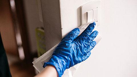 Gloved hand wiping a light switch with a disinfecting wipe
